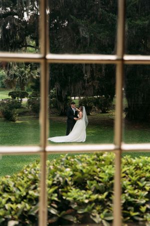 View through window panes of a couple dancing in a lush garden with Spanish moss draped trees.