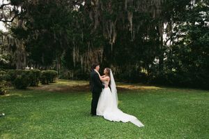 Wedding couple walks together beneath Spanish moss covered oak trees at a romantic outdoor venue in nature.