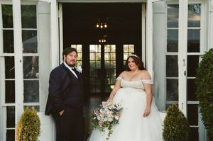 Bride and groom pose at elegant venue entrance with French doors and topiaries on their wedding day.