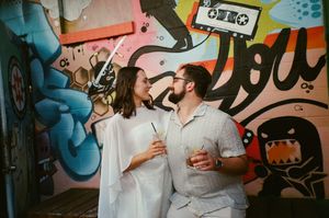 Couple smiling at each other holding drinks in front of colorful graffiti wall art.