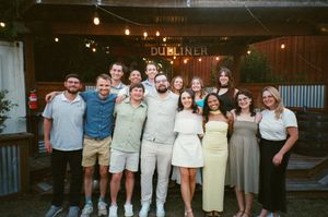 Group of young adults smiling together outside The Dubliner bar with string lights in background.