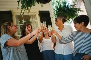 Four women toasting with champagne glasses outdoors, celebrating together under lush green hanging plants.
