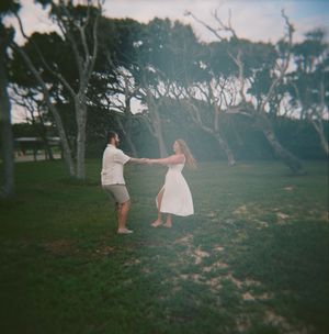 Two people dance and spin together on a grassy hillside at sunset, creating a dreamy silhouetted scene.