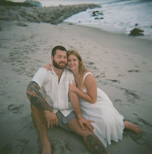 A romantic couple relaxes together on a sandy beach at sunset creating intimate portraits along the shoreline.