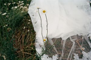 White flowing fabric on grass with delicate yellow daisies growing alongside it.