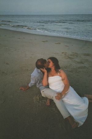 Romantic couple embracing and dancing on a misty beach at dusk with ocean waves in the background.