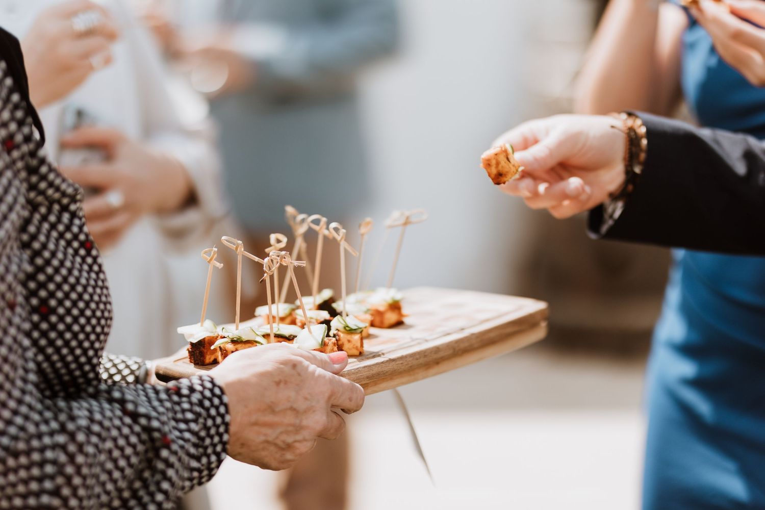 Close-up shot of hands holding canapé containers on a wooden surface with blurred background.