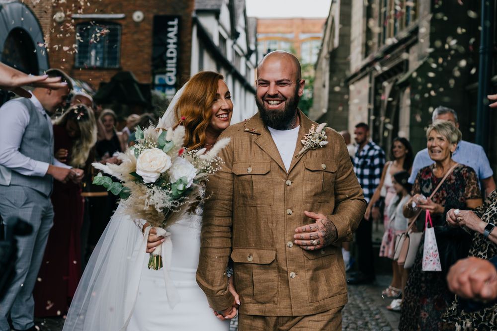 A happy couple celebrates their wedding day on a cobblestone street with brick buildings in the background.