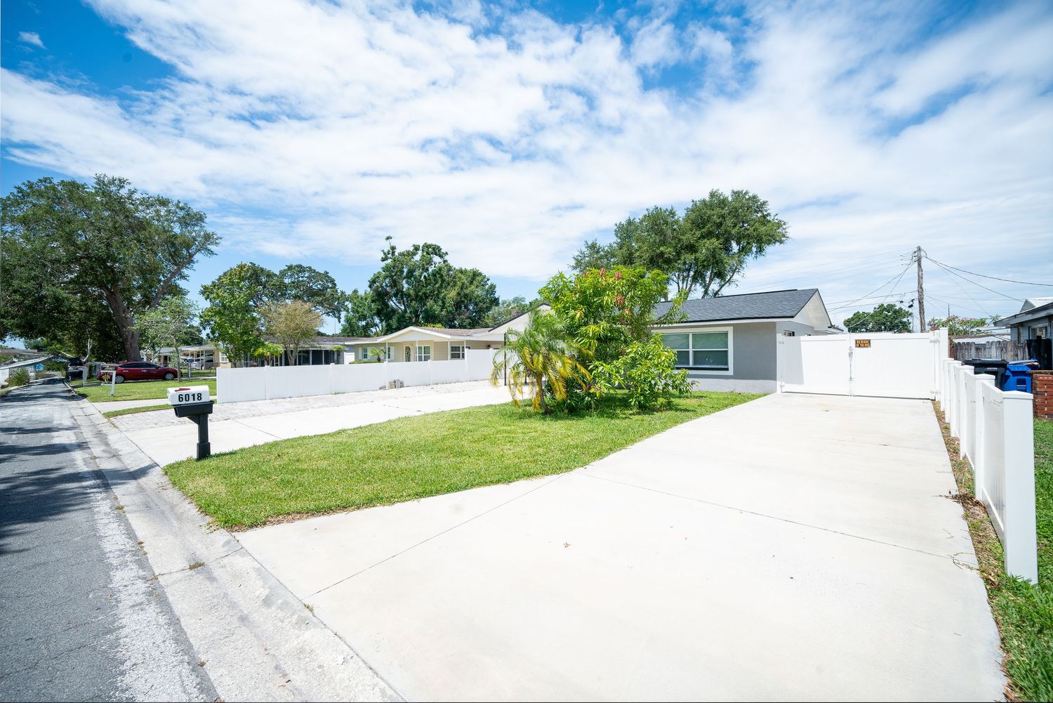 A panoramic street view showing a suburban neighborhood with paved roads, green lawns, and houses under a blue cloudy sky.