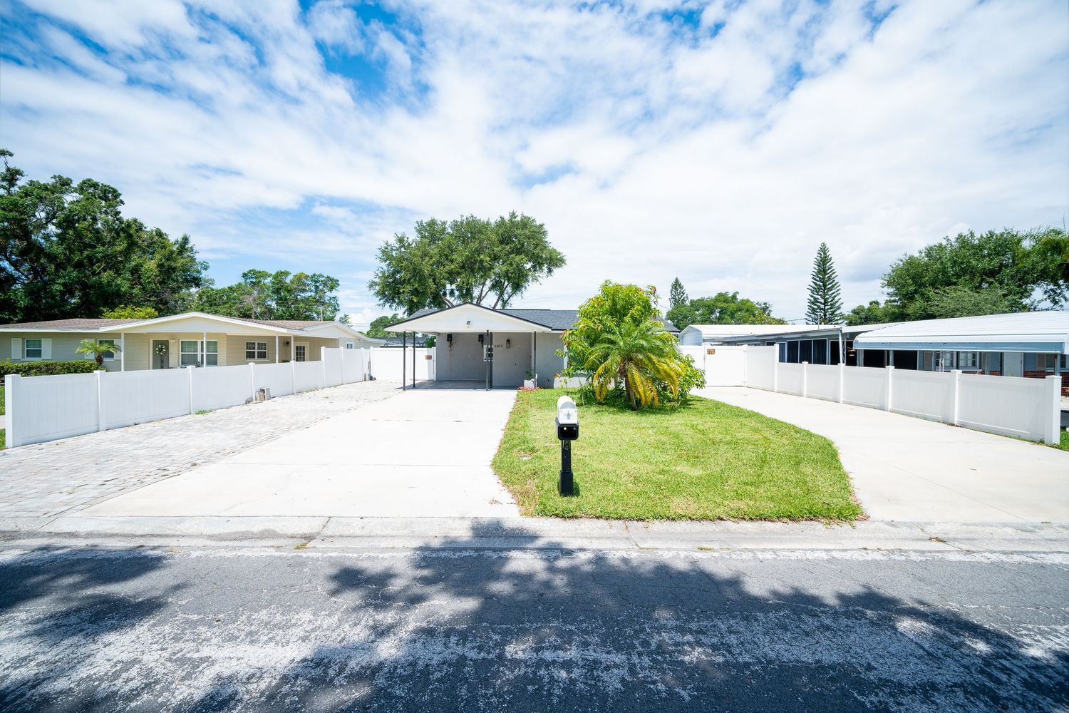 Mobile home park with white manufactured homes and green lawns on a curved road under blue cloudy skies.