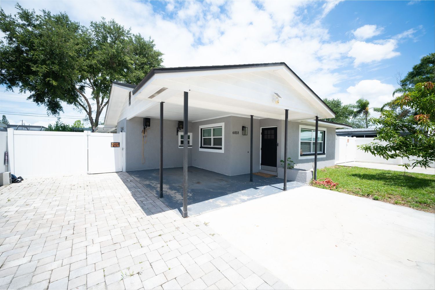 Modern single-story home exterior with white brick driveway and covered front porch under bright blue sky.