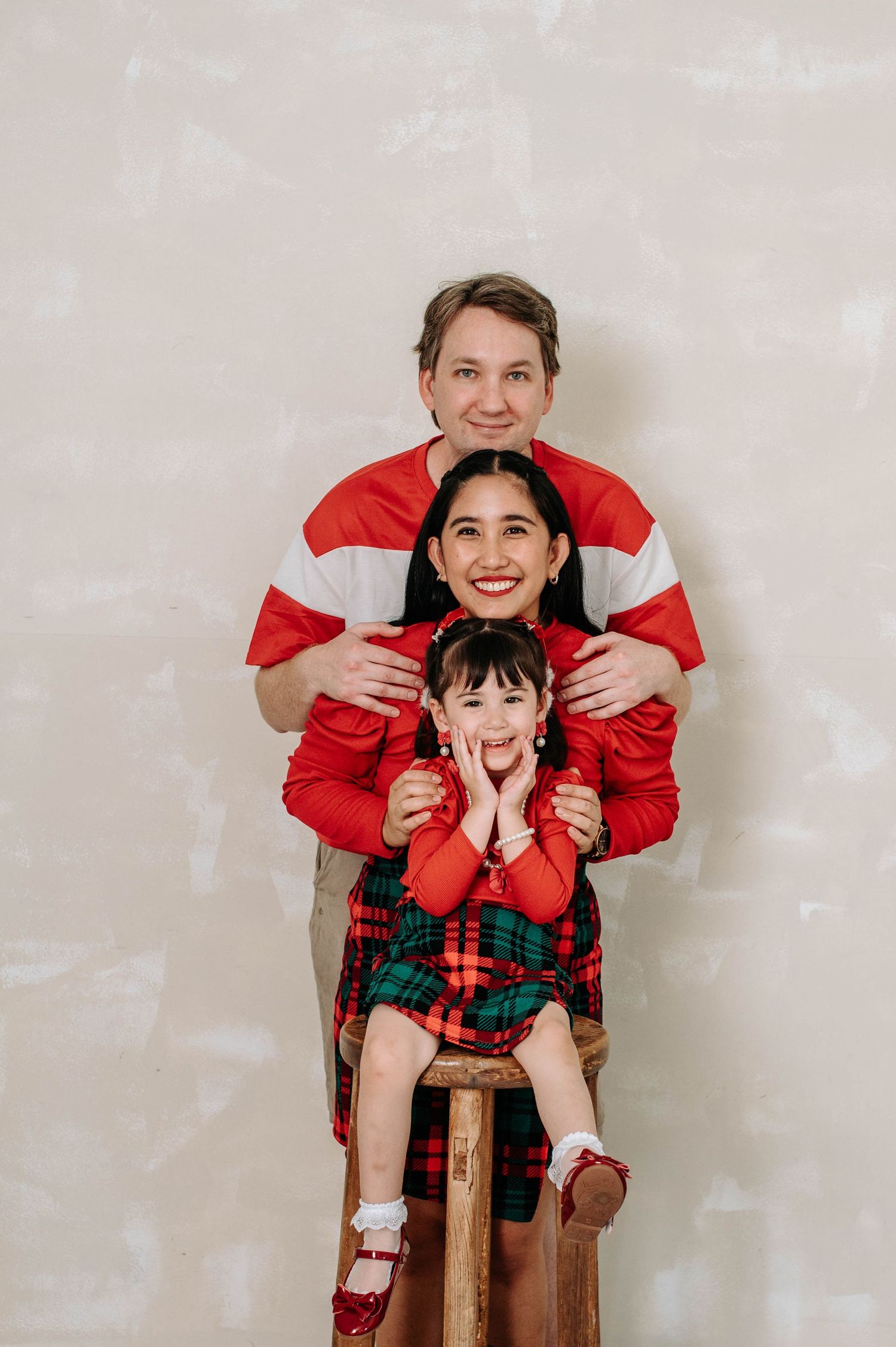 Family in matching plaid and red holiday outfits pose playfully against neutral wall in progressive candid shots.