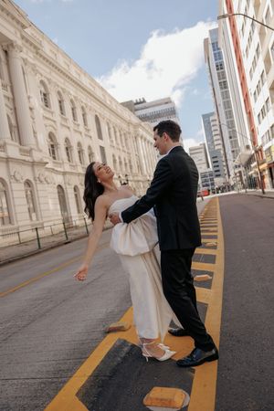 A couple dances romantically on a city street lined with elegant white stone architecture and yellow painted lines.