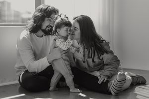 A family shares a tender moment together while sitting on the floor near a window in black and white.