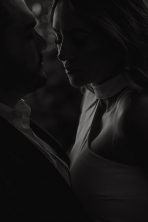 A romantic black and white portrait of a couple in intimate proximity, captured in dramatic shadows and low light.