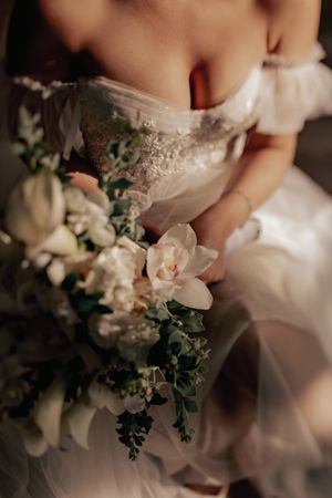 Close-up detail of a white wedding dress bodice with delicate lace and a romantic bouquet of white orchids and greenery.