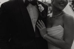 Black and white close-up wedding photo showing couple's formal attire with tuxedo, pearl necklace and strapless dress.
