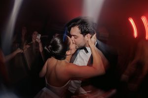 A couple shares a passionate kiss on the dance floor at a dimly lit wedding reception with red lighting.