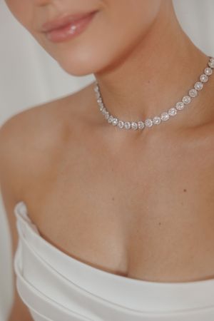 Close-up of an elegant diamond tennis necklace worn with a white top, showcasing delicate sparkle and luxury.