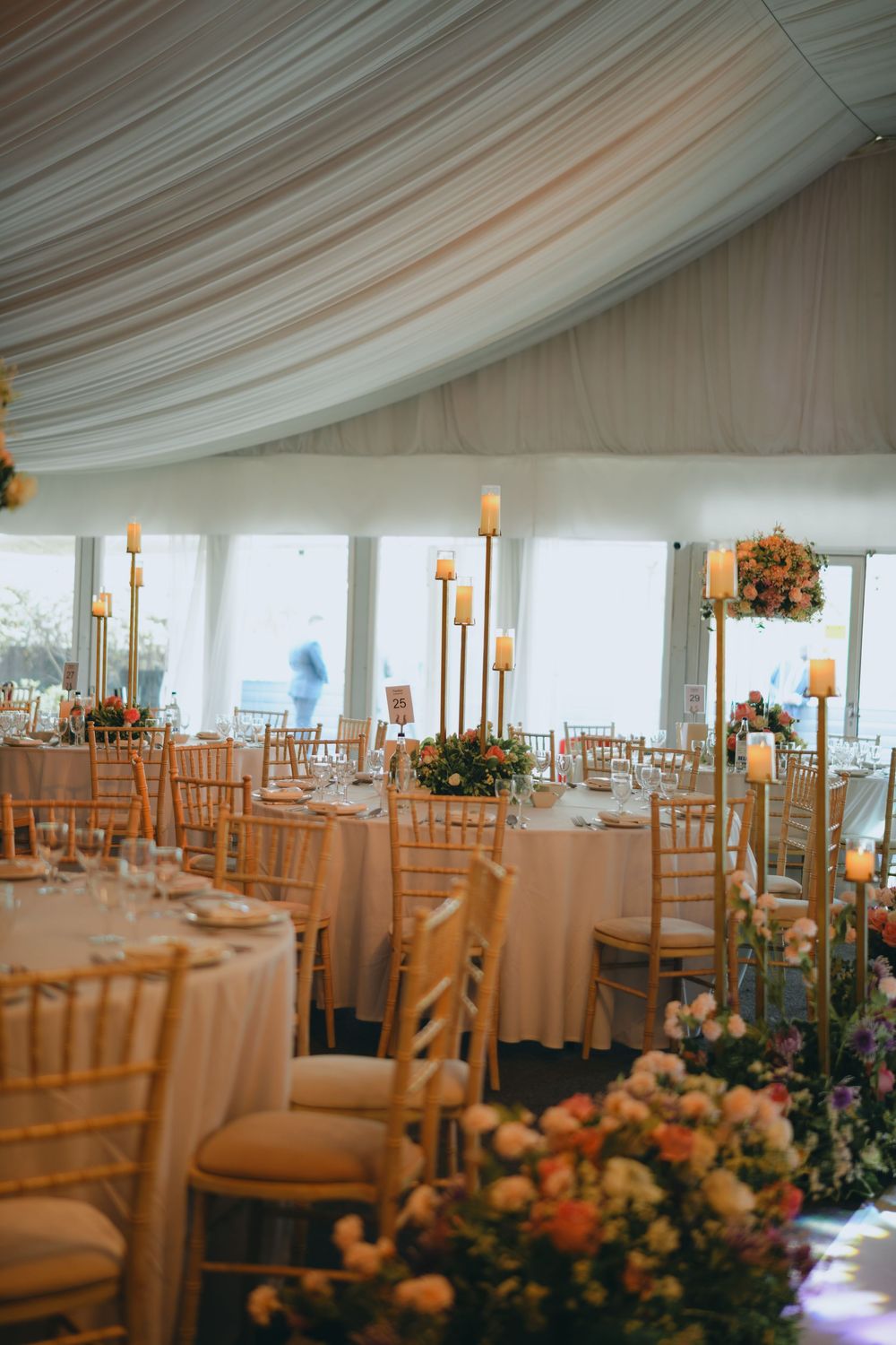 White draped tent ceiling over elegant wedding reception tables with wooden chairs and peach floral centerpieces.