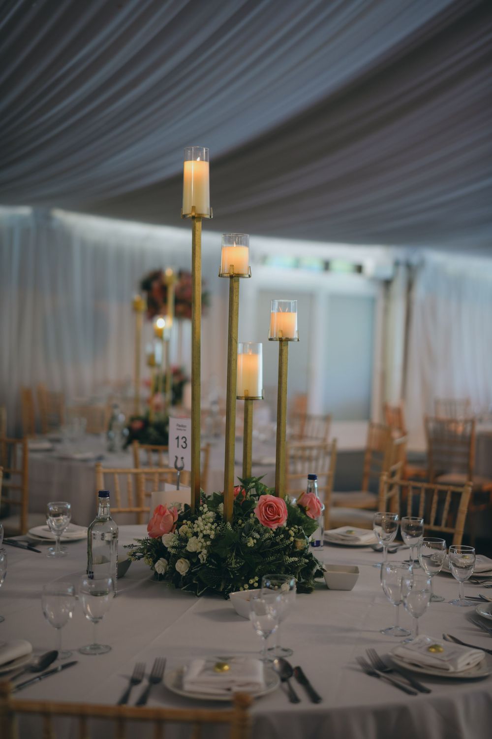 Romantic table setting with tall gold candlesticks and pink rose centerpiece at an elegant wedding reception.
