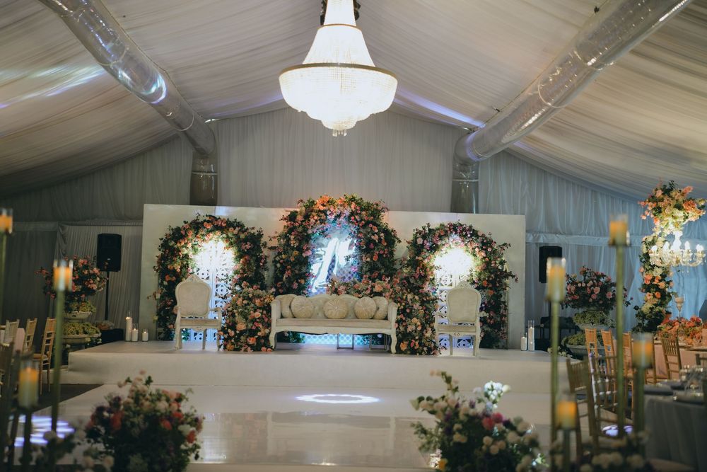 Elegant wedding venue with floral arches and crystal chandelier features white draping and raised stage platform.