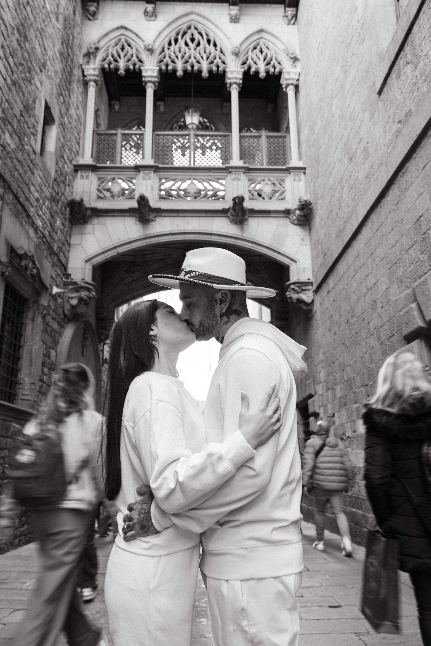 Couple in white outfits exploring historic Gothic architecture with other tourists visible.