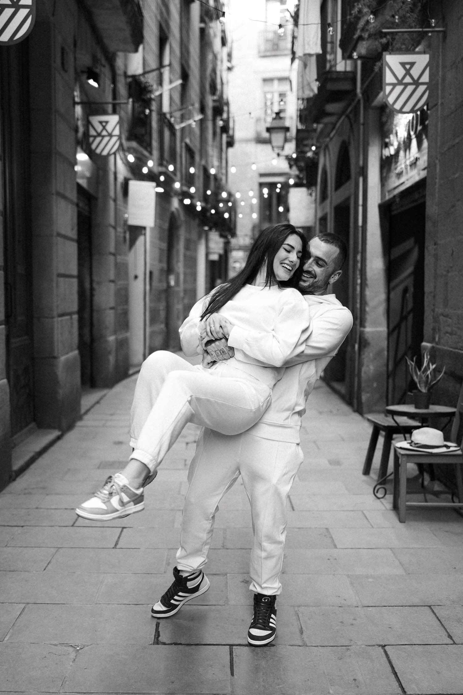 Black and white photo of a couple dancing playfully in a historic alley.