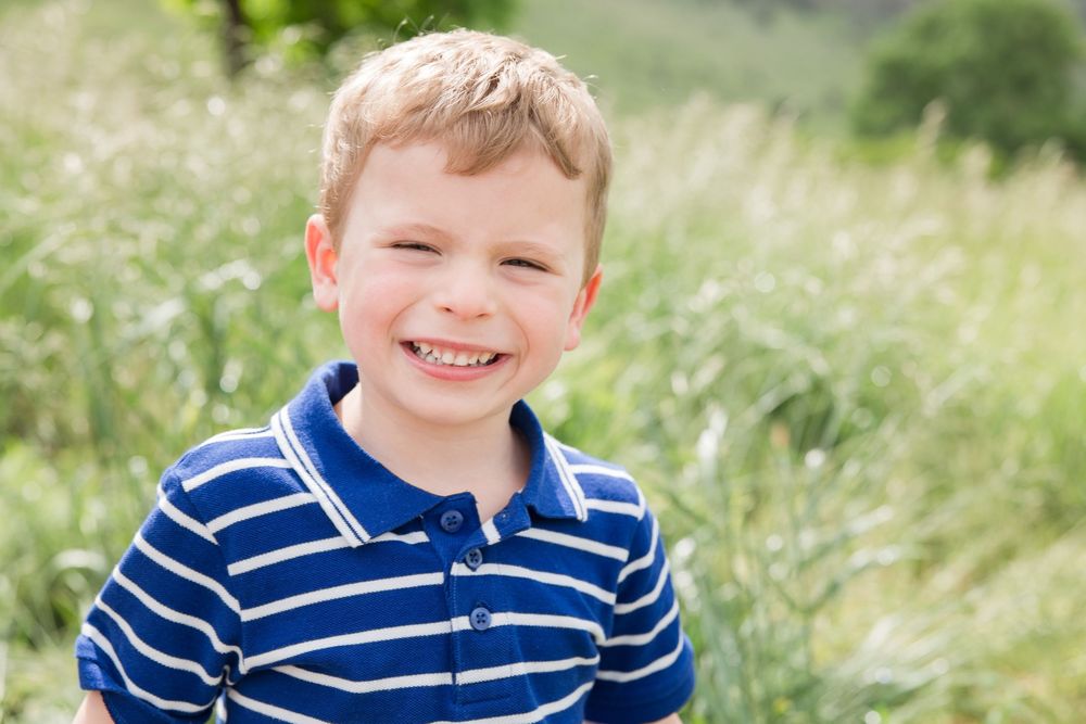Young boy in a blue striped polo shirt smiling in a field of tall grass.