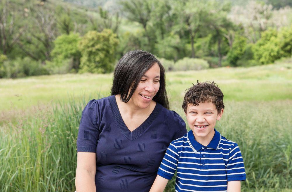 Parent and child sitting together in a grassy meadow surrounded by green hills.