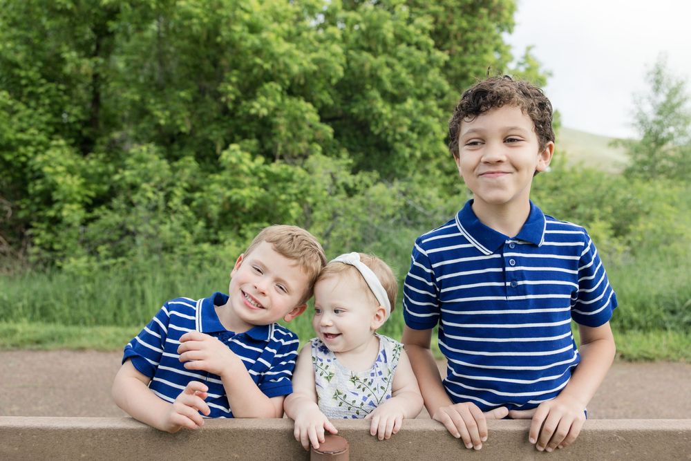 Three siblings sitting together on a wooden bench outdoors.