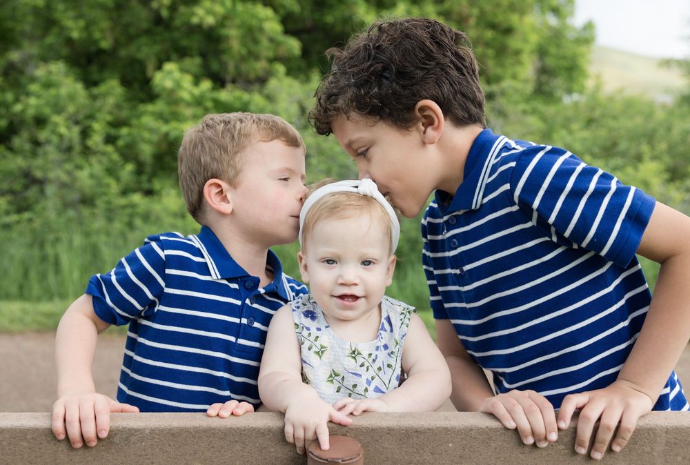 Three siblings sharing a close moment together on a wooden bench.