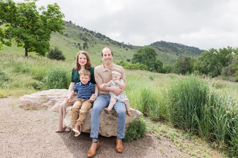 Family sitting together on a bench surrounded by green hills and natural scenery on a sunny day.