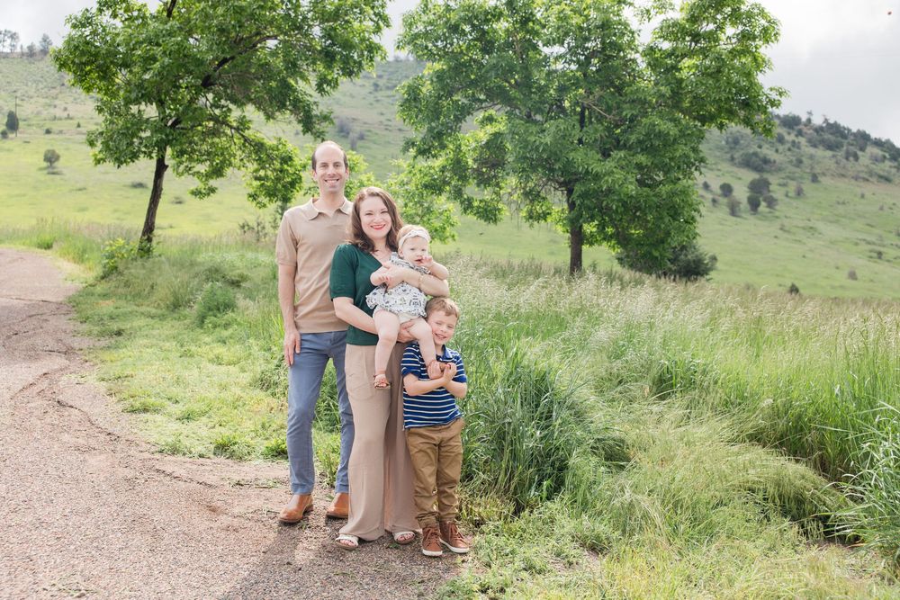 Family poses together on a dirt trail surrounded by green hills and trees.