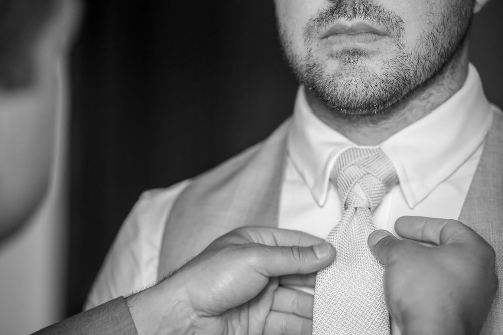 Close-up black and white photo of someone adjusting a light colored necktie while wearing a white dress shirt.
