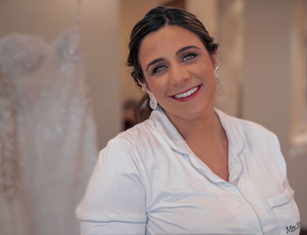A medical professional in a white uniform smiles warmly while standing inside a healthcare facility.