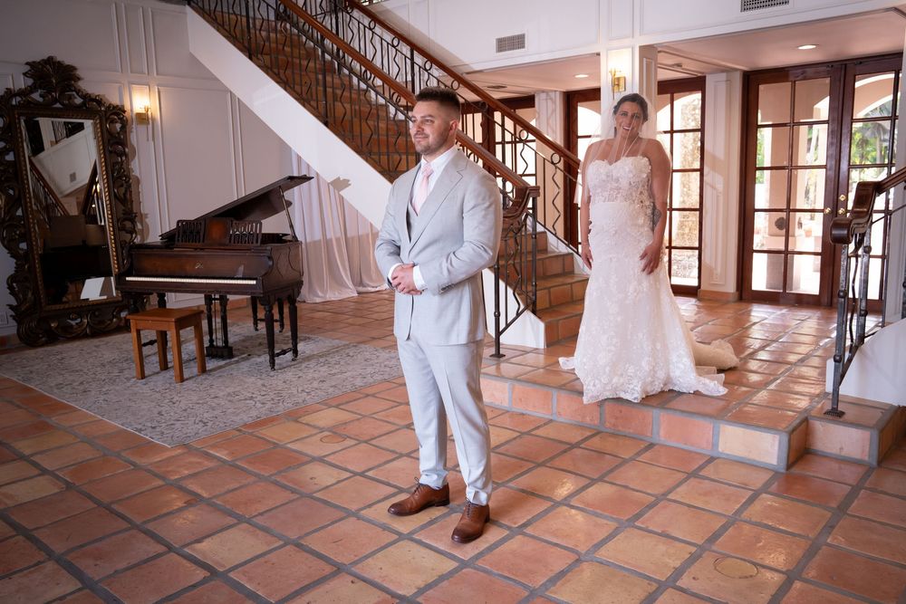 Two toddlers in white clothing dance and play in a sunlit room with terracotta tile floors and large windows.