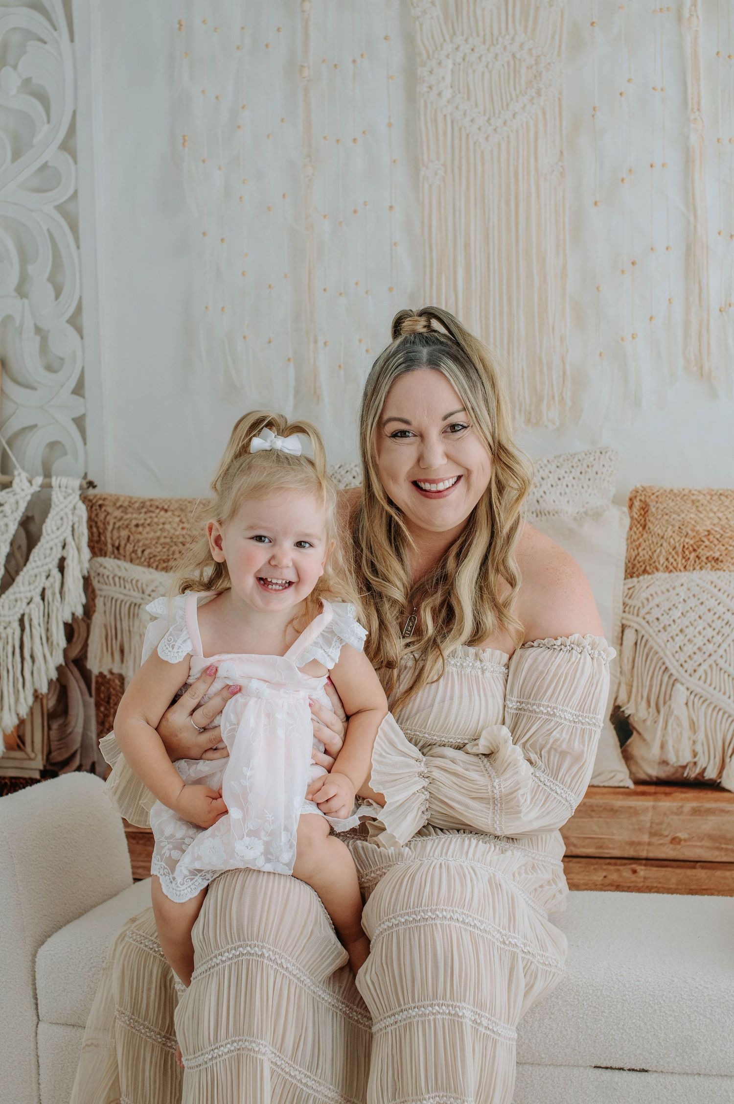 Two figures in coordinating neutral outfits share a joyful moment on a couch with decorative macrame pillows.