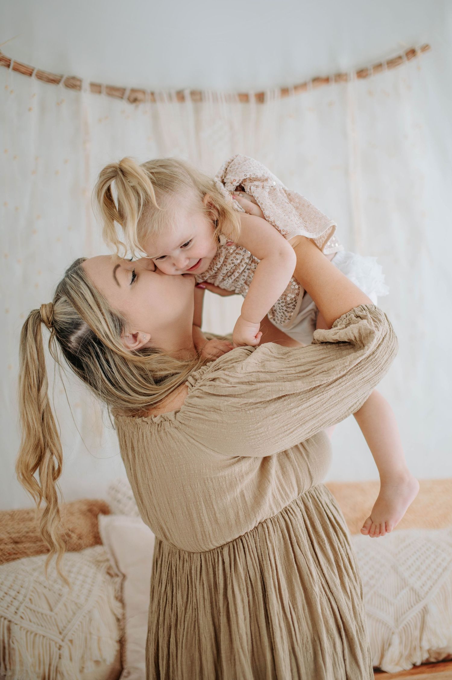 A tender moment between a parent and baby wearing beige clothing on a light-colored background.