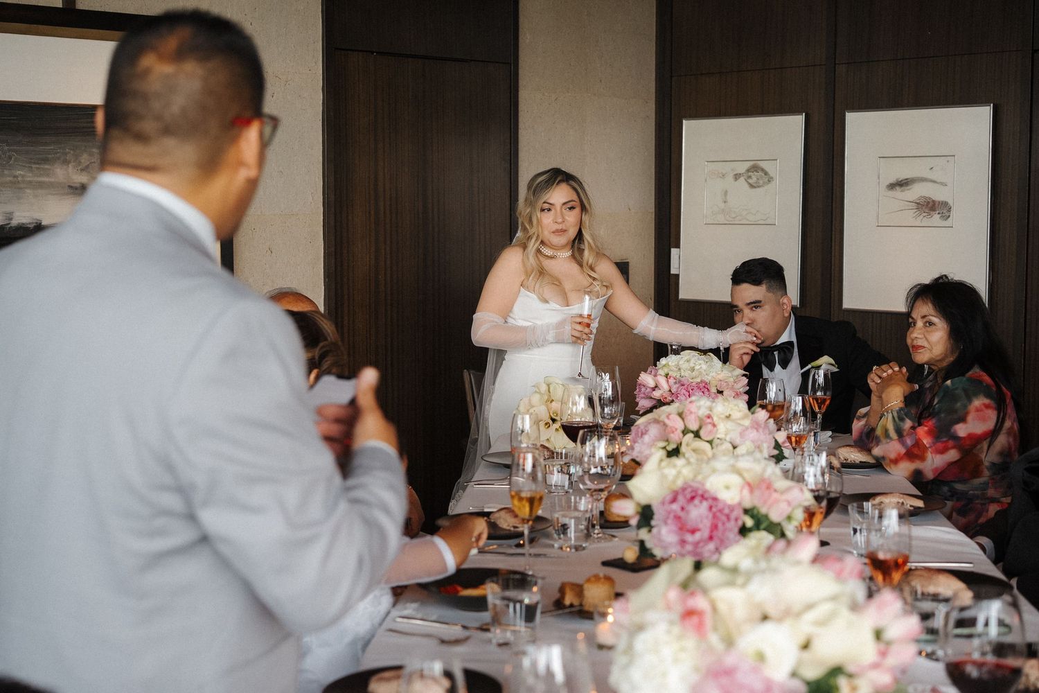 People gathered at an elegant dinner reception with pink floral centerpieces and framed artwork on the walls.