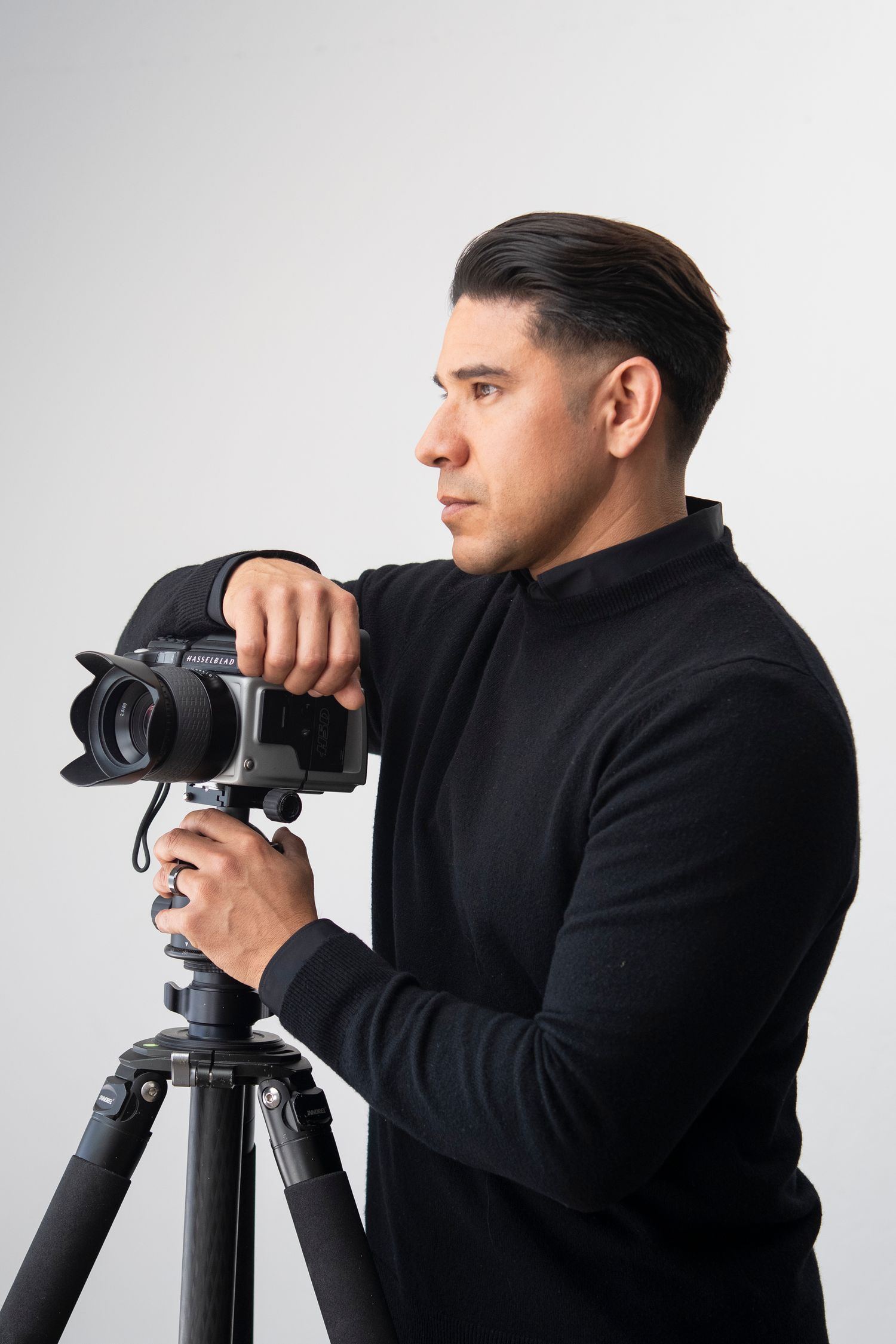 Photographer in black turtleneck working with camera on tripod against white background.