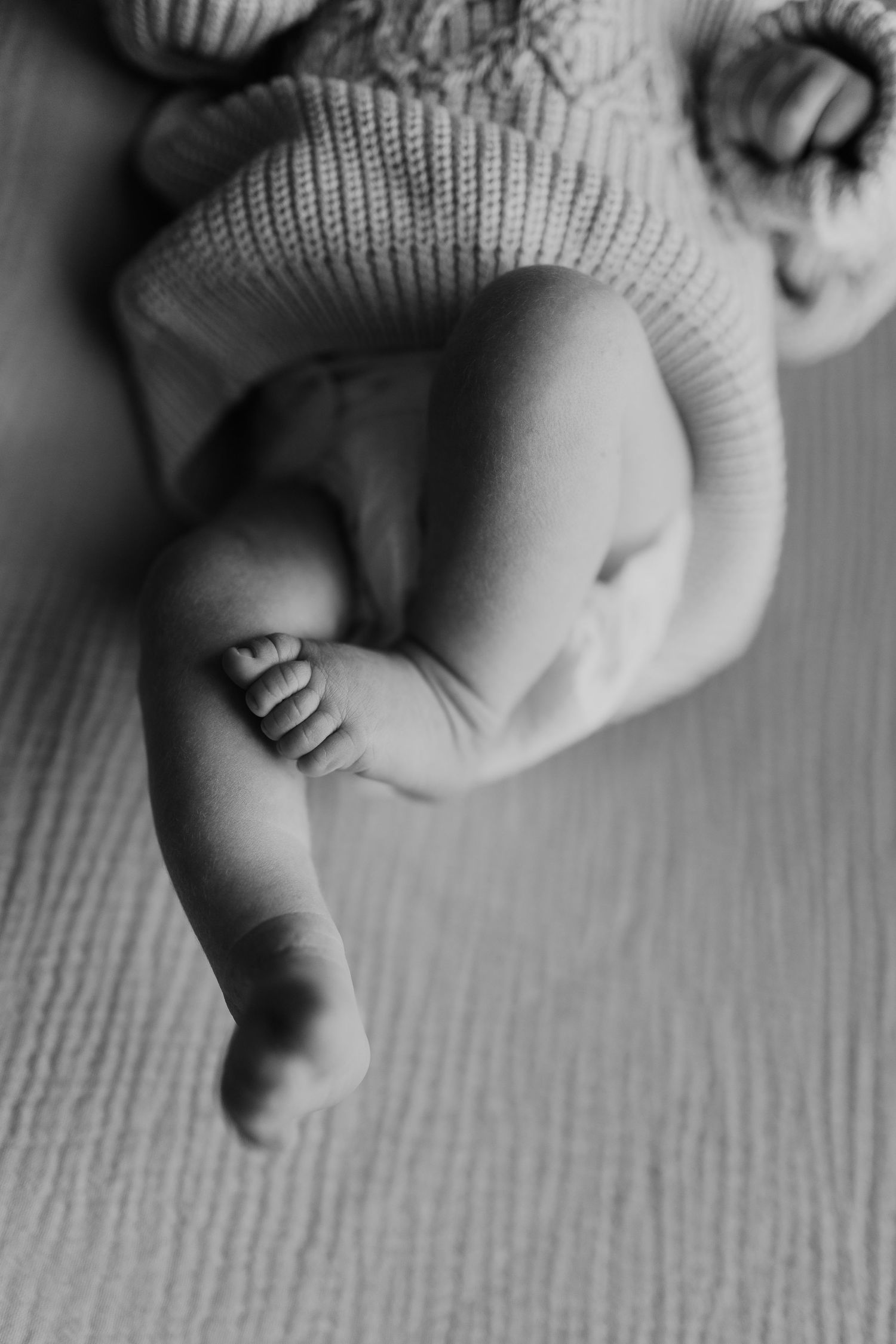 Black and white close-up of tiny baby feet in soft knit clothing on textured surface.