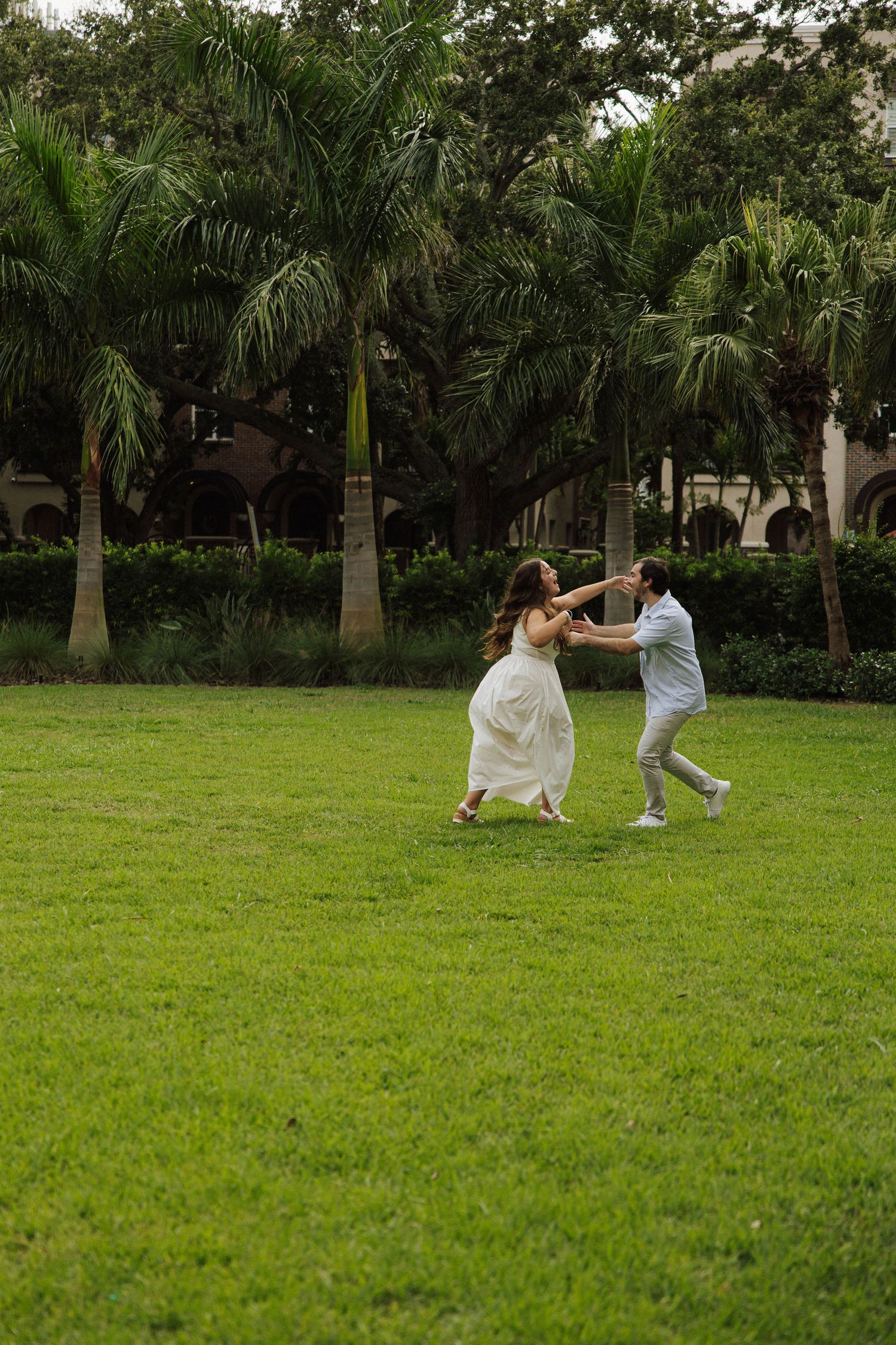 A couple dancing together on a green lawn surrounded by tall palm trees in a tropical garden setting.