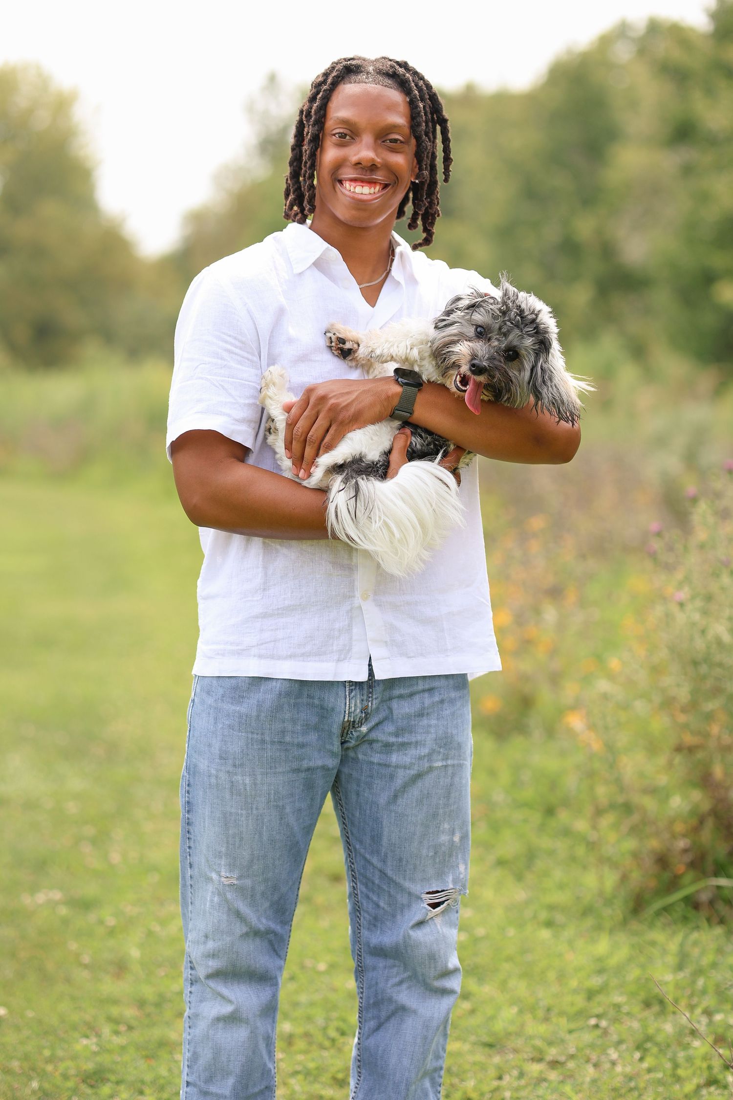 A person in white holding a small gray dog during an outdoor portrait session.