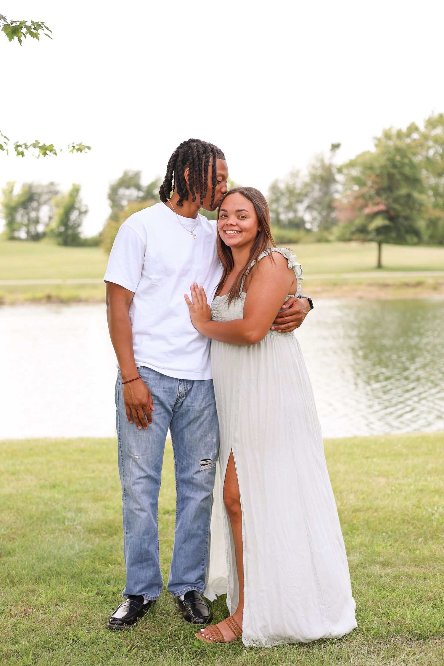 A romantic couple pose by a lake in coordinating white outfits.