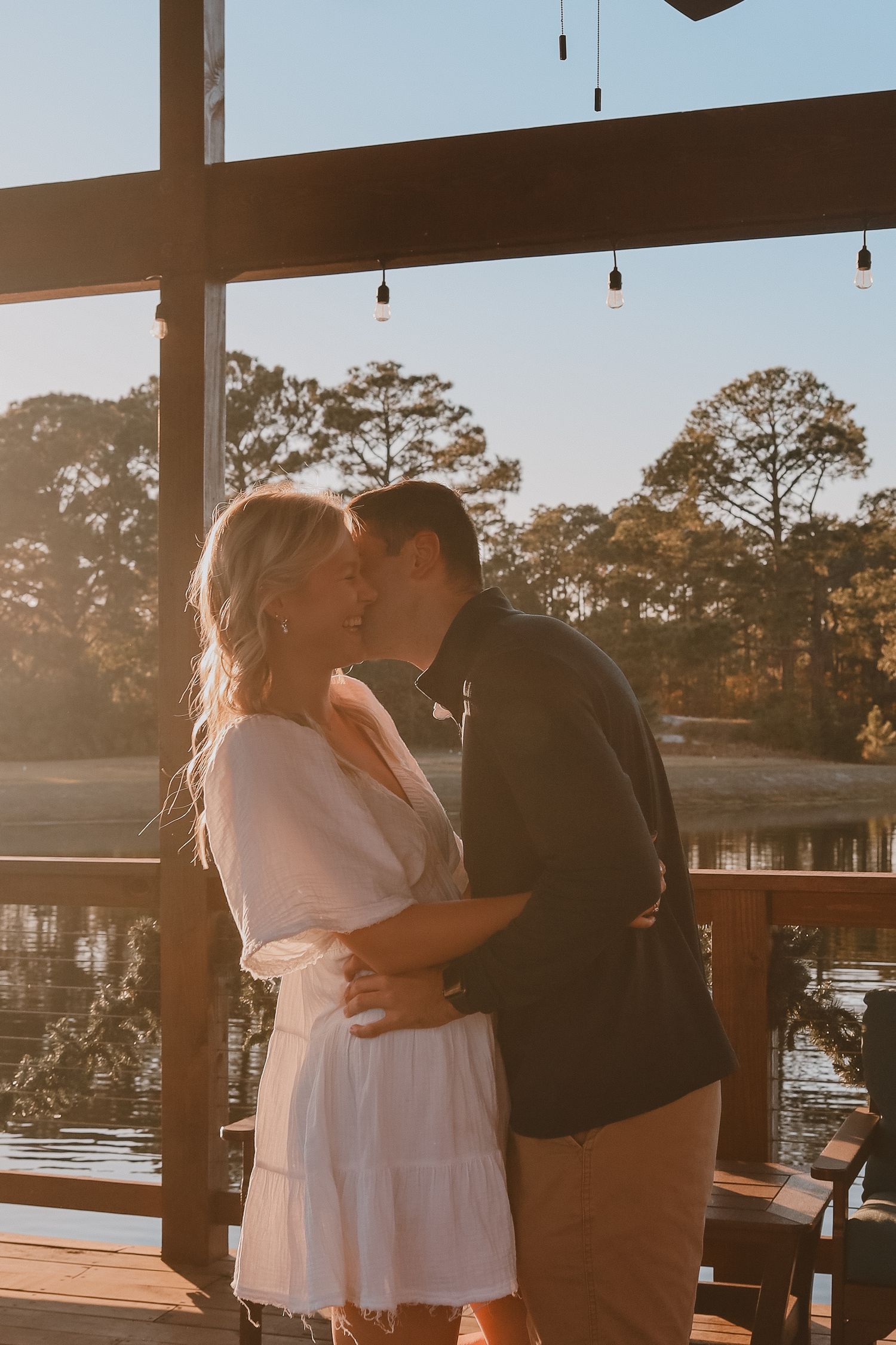 Happy couple sharing a kiss on waterfront deck bathed in warm sunset light.