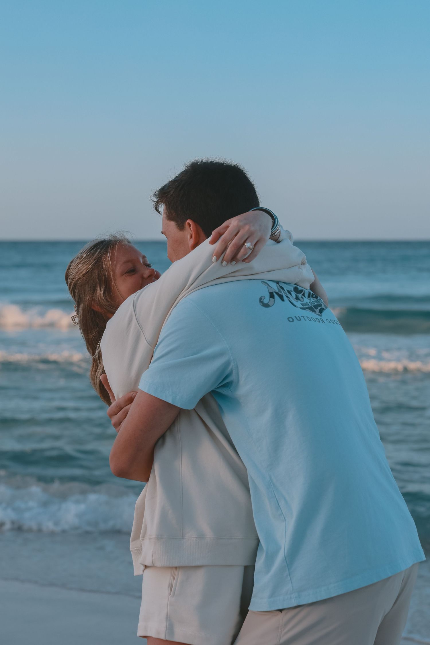 Couple sharing a warm embrace on a beach at dusk with ocean waves.