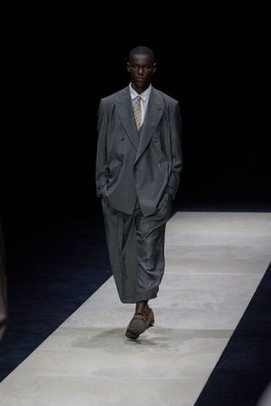 Classic charcoal gray suit styled with casual elegance on illuminated fashion runway.