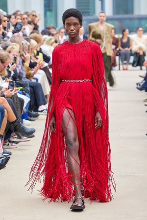Dramatic red fringed dress with belt detail presented during outdoor fashion show.