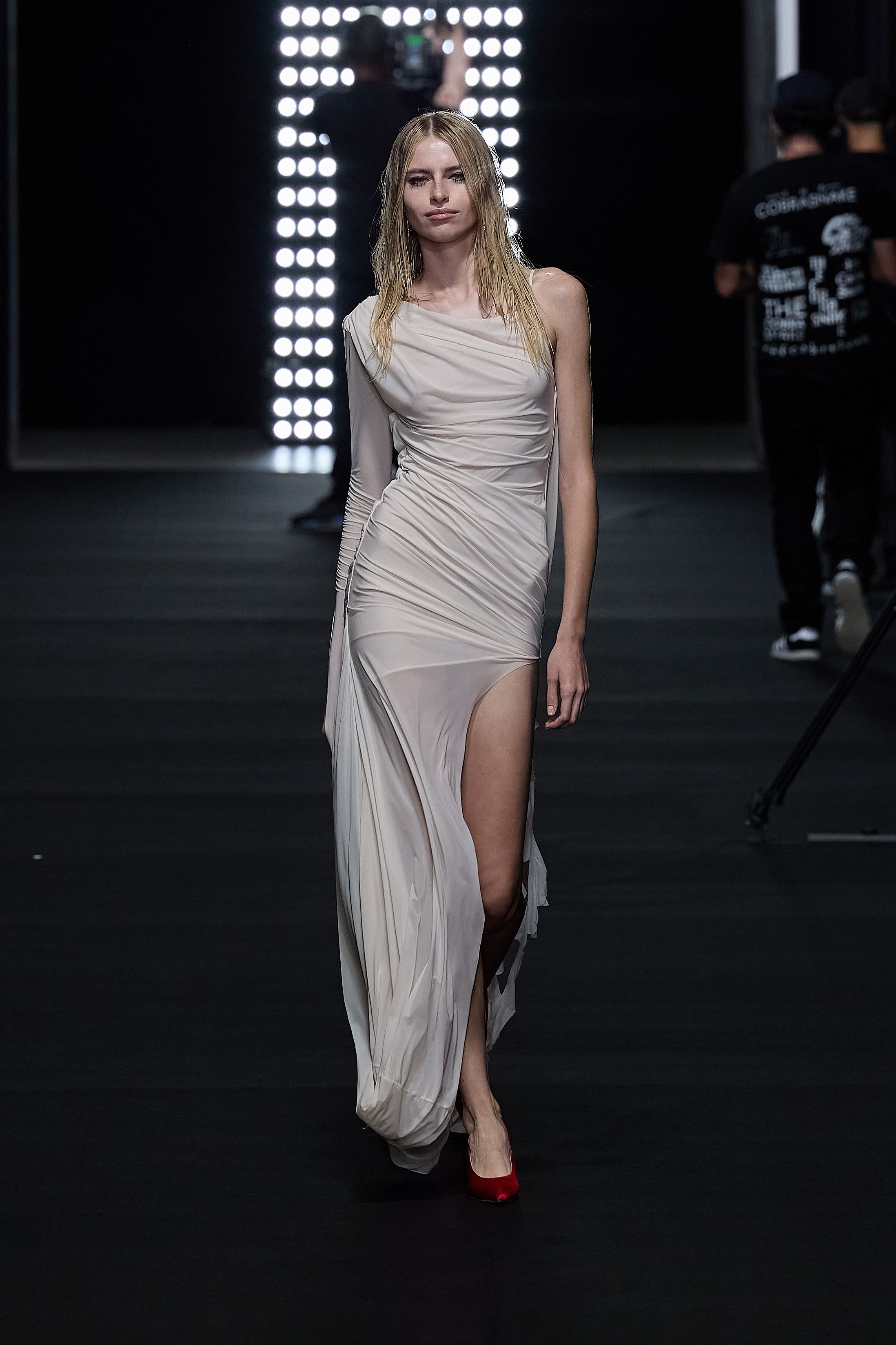 Model walks runway in black lingerie dress with dramatic white fur coat.